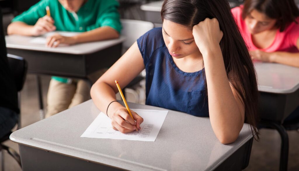 Girl student sitting at a desk taking an exam in a classroom, focused on answering test questions, representing education, academic success, and exam preparation.